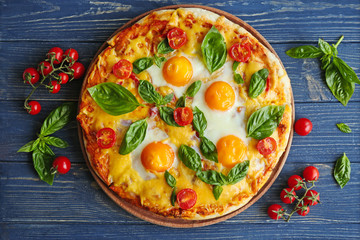 Margarita pizza with basil leaves and egg on wooden table, top view