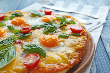 Margarita pizza with basil leaves and egg on wooden table closeup