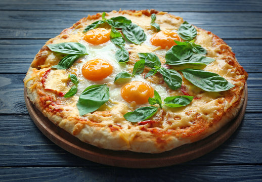 Margarita pizza with basil leaves and egg on wooden table closeup