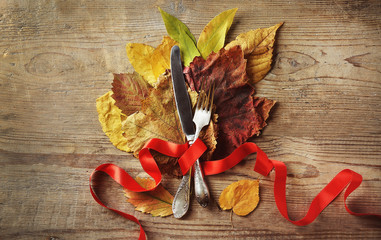 Autumn composition of leaves, ribbon, knife and fork on wooden background. Thanksgiving day concept