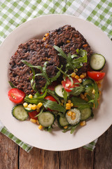 Vegetarian food: black bean burgers and a salad of fresh vegetables close-up. Vertical top view

