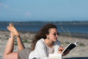 Woman with long curly hair reading a book at the beach