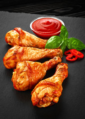 Fried chicken legs with ketchup, chili pepper and basil on a dar