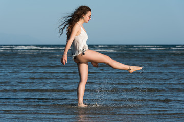 Naklejka premium Woman with long curly hair wear bikini and shirt, standing in sea and kick the water. Sea and sky as background