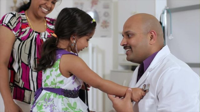 A cute little Indian girl with her mother uses a stethoscope to listen to the heart beat of her kind pediatrician.