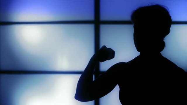 Silhouetted image of a muscular woman working out with a small hand weight or dumbbell.
