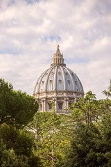Fototapeta na wymiar The dome of the famous St Peter's Basilica in The Vatican, seen through the trees on a cloudy summer's day, in a vertical format.