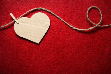 Heart from cardboard on rope with clothespin on red background with the gradient effect. Valentine's day