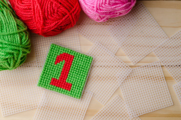 Plastic Canvas, hand made with red yarn number on wooden backgro