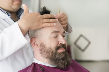 Barber makes a mohawk hairstyle of a adult bearded man
