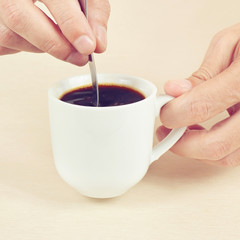 Hands mixing with a spoon of black coffee in the cup, gently toned