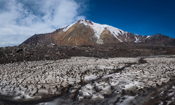 Icy glaciers on the slopes of Tolbachik Volcano viewed over a field with snow covered with sand and ash, Kamchatka, Russia.