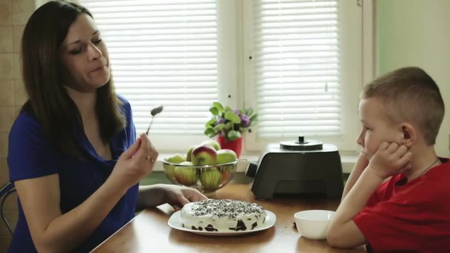A pregnant young mother and little son have cooked cake and are going to try it.