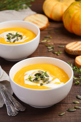 Pumpkin cream soup with cream and pumpkin seeds on wooden background, selective focus