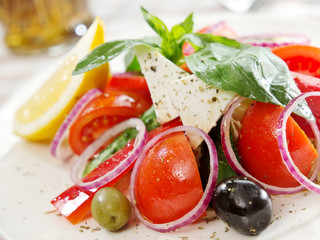 Greek salad with tomatoes, feta cheese slice, olives, onion and basil leaves. greek cuisine