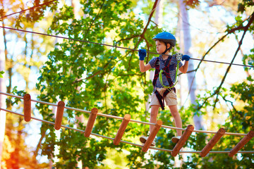 young boy passing the cable route high among trees, extreme sport in adventure park