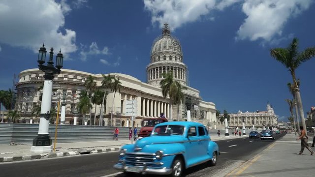 View to central touristic street of Havana. Colorful retro cars are passing by the Capitol and alley with palms at summer sunny day.