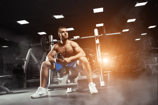 Young muscular man sitting with a bottle of water in the gym