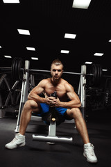 Naklejka na ściany i meble Young muscular man sitting with a bottle of water in the gym