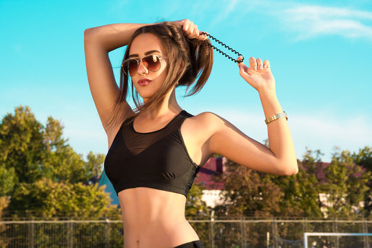 Young cool woman holding hair. Fashionable girl in a sports tank top and sunglasses on the background of azure sky. Swag girls. Swag style. 