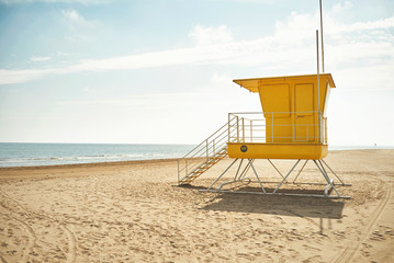 Yellow lifeguard post on an empty sandy beach with the background of blue sky with clouds and the sea
