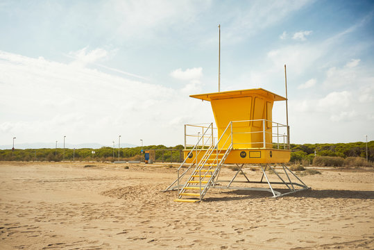 Footprints on an empty beach around a bright yellow lifeguard post Commercial image