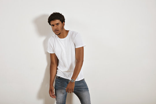 Young serious looking black model in jeans and blank white t-shirt moving away from the camera against a white wall