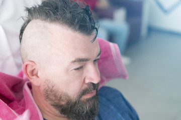 Male barber wipes head with pink towel of a adult man with a mohawk