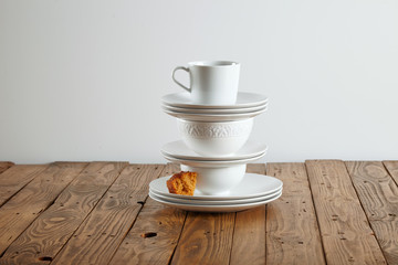 Similar but different white t-cups perched on top of each other with a tiny bit of light brown sponge cake on a saucer