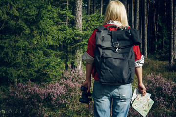 Young active woman tourist standing in a clearing in the woods with a backpack, holding binoculars...