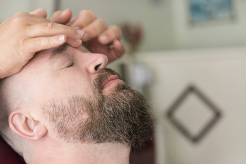 Obraz premium Male barber doing massage for the face of a adult bearded man with a mohawk