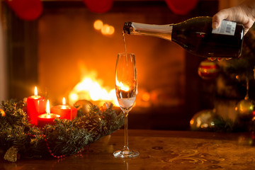 Pouring champagne in glass on table decorated for Christmas