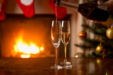 Two glasses of champagne being filled . Christmas tree and burni