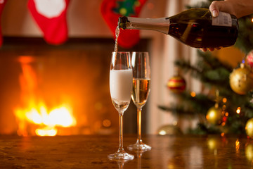 Person filling glasses with champagne. Burning fireplace and dec