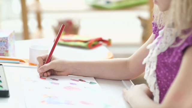 Profile of a beautiful little girl with long white hair. Girl sitting at the desk and drawing with colored pencils. Children's drawing. The child is busy drawing. Portrait of a drawing girl