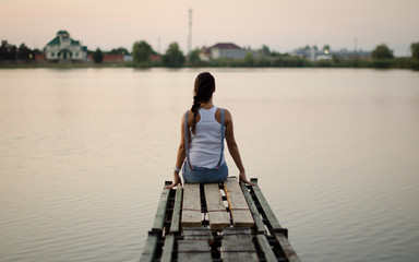 Fototapeta na wymiar young girl sitting on the bridge from the back