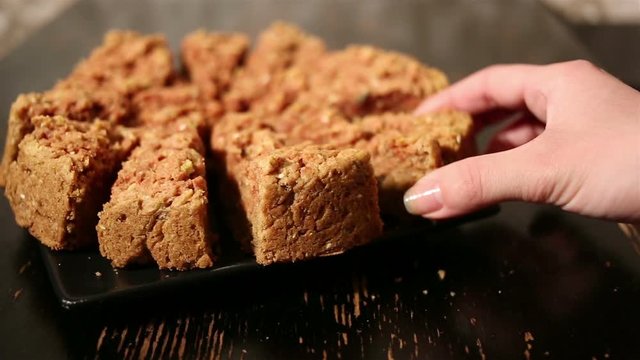 Girl's hand takes a piece of oat cake from black plate on a black table.