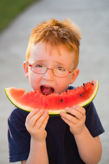 Happy boy with red hair in glasses eating watermelon