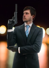 Secret agent in suit holds pistol with silencer in hand at night.