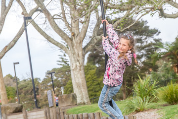 Happy Child blond girl rids on Flying Fox play equipment in a ch