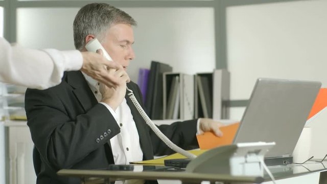 A man on his office desk phone gets no consideration from a coworker who needs her paperwork.  Canon C300