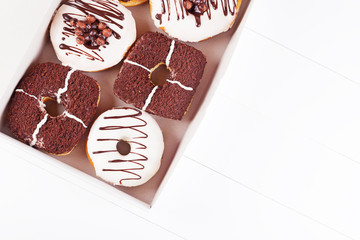 Chocolate delicious donuts with sprinkles and glaze in a box on a white wooden background. Top view with copyspace