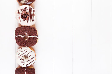 Sweet delicious donuts with chocolate, sweet glaze and sprinkles in a row on a white wooden background. Top view with copyspace