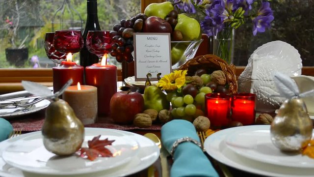 Colorful rustic style Thanksgiving table with fruit, candles, and cornucopia centerpiece in front of a garden window on a rainy day, close up static.