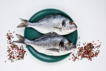 Raw dorado fish on yellow plate with peppercorns on white table. Top view, copy space 