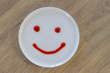 smiley face of tomato source on white plate over wooden backgrou