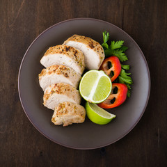 Sliced lime pork tenderloin with vegetables salad on dark wooden background top view.