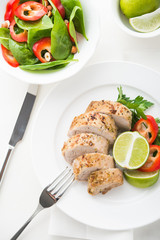Sliced lime pork tenderloin with spinach salad on white background top view.