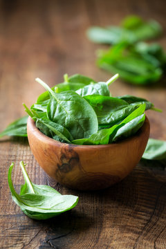 Spinach leaves in wooden bowl against dark rustic background