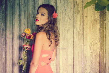 Attractive young brunette woman with flower in hair talking on mobile phone at wood wall copyspace background